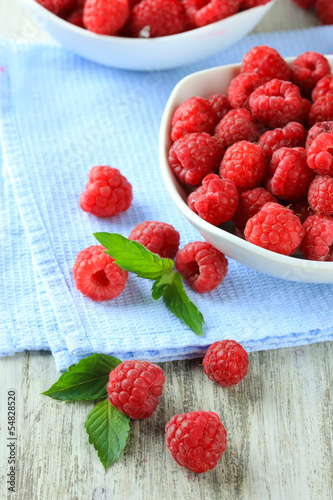 Ripe sweet raspberries in bowls on wooden background