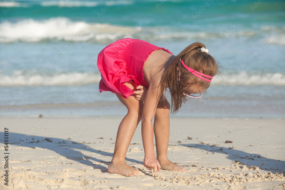 Fototapeta premium little cute girl draws on the white sand at tropical beach