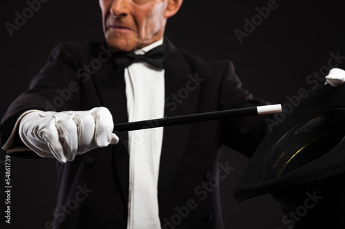 Magician with black suit and hat holding a magic stick. Studio s