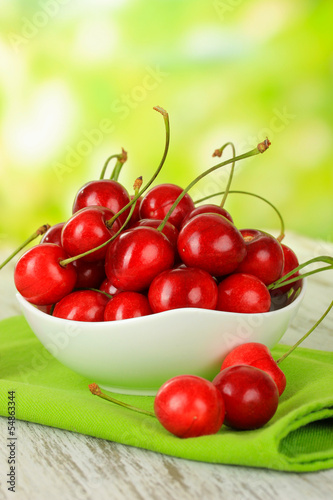 Cherry berries in bowl on wooden table on bright background