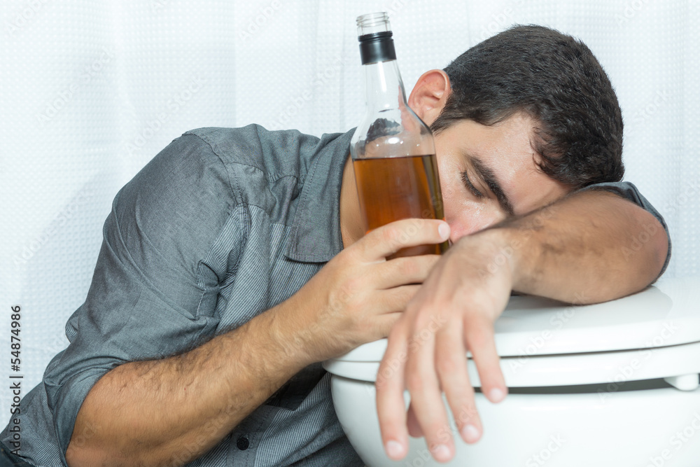 Drunk man sleeping on the toilet and holding a bottle Stock Photo