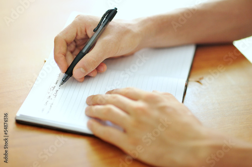 student hand with a pen writing on notebook