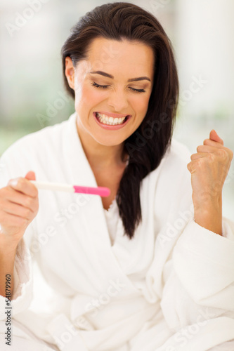 excited young woman holding positive pregnancy test
