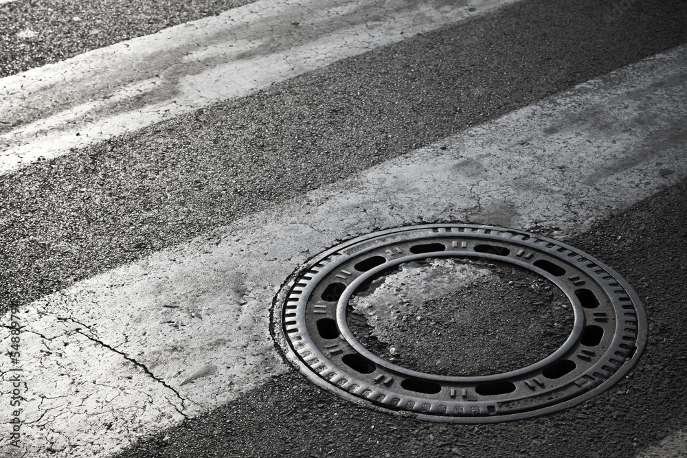 Sewer manhole cover on dark asphalt road