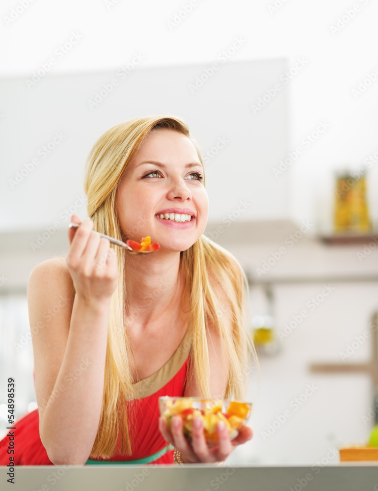 Happy young woman eating fresh fruits salad in kitchen Happy young woman eating fresh fruits salad in kitchen
