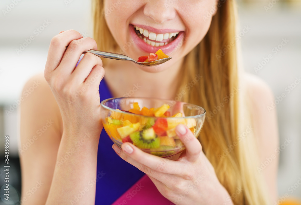 Closeup on young woman eating fresh fruits salad in kitchen Closeup on young woman eating fresh fruits salad in kitchen