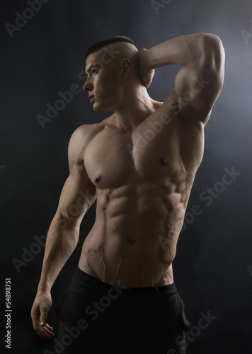 Young sexy man with athletic body posing on black background.