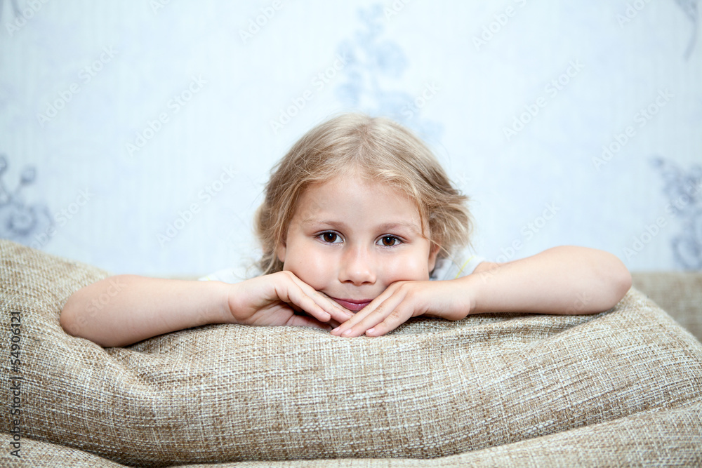 Small child sitting on sofa with hands clasped on pillows Small child sitting on sofa with hands clasped on pillows