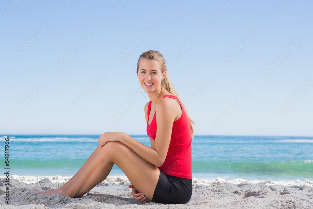 Fit blonde sitting on sand smiling at camera Fit blonde sitting on sand smiling at camera