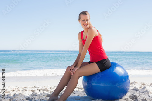 Athletic young woman sitting on exercise ball looking at camera