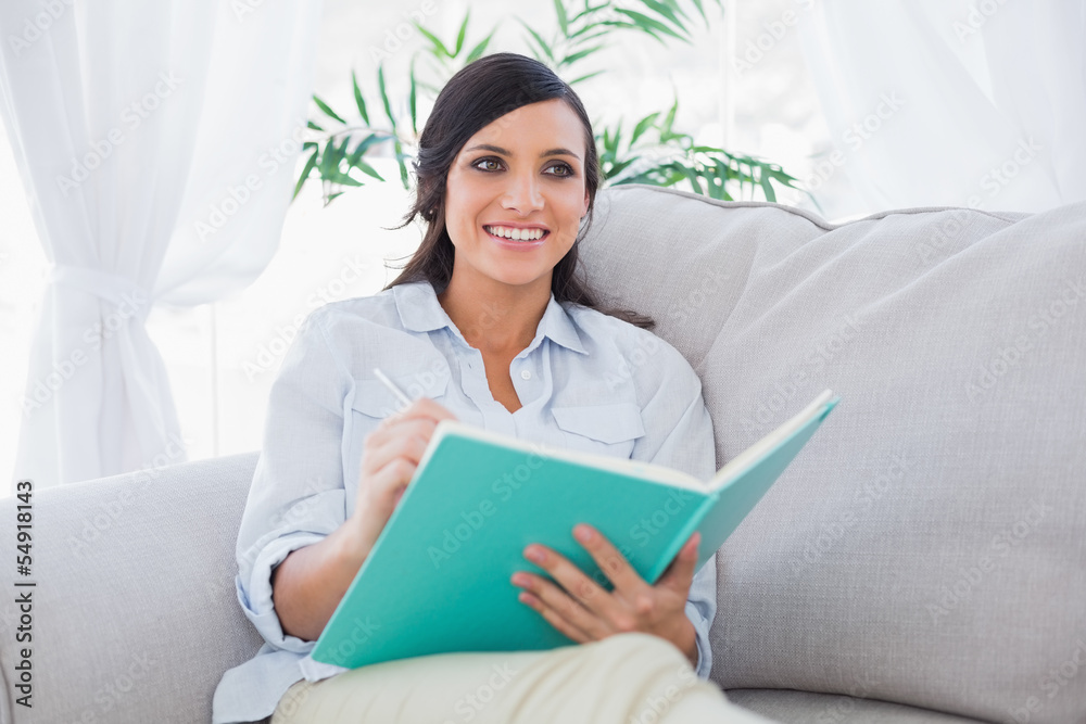 Happy brunette writing while sitting on the sofa Happy brunette writing while sitting on the sofa
