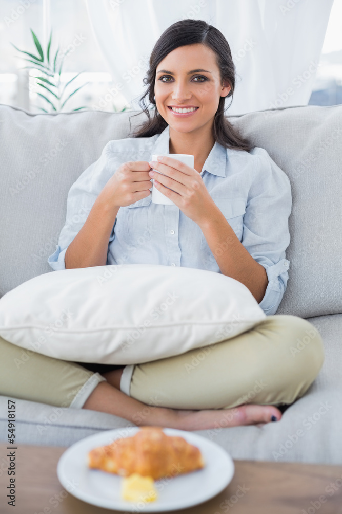 Cheerful woman on sofa drinking coffee and having croissant Cheerful woman on sofa drinking coffee and having croissant