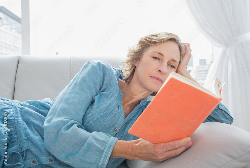 Content blonde woman relaxing on her couch reading book Content blonde woman relaxing on her couch reading book