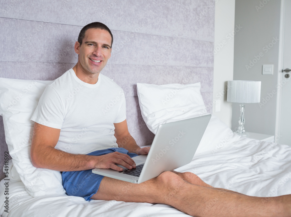 Happy man using laptop on bed Happy man using laptop on bed