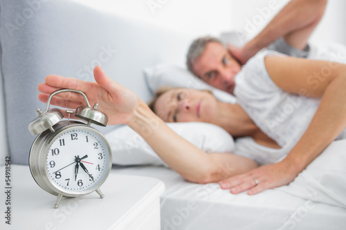 Wife turning off alarm clock as husband is covering ears