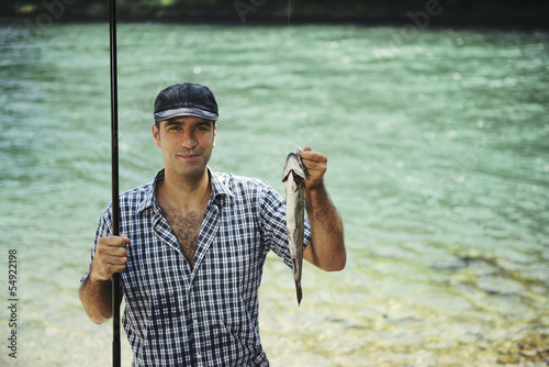 man fishing on river and showing fish to the camera