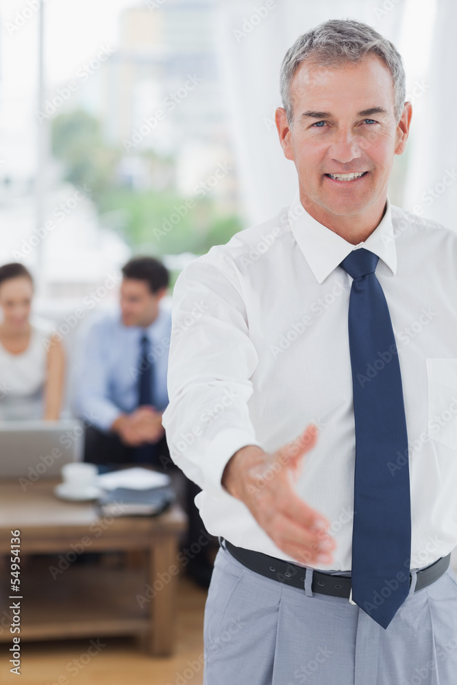 Executive standing on foreground holding out his hand Executive standing on foreground holding out his hand
