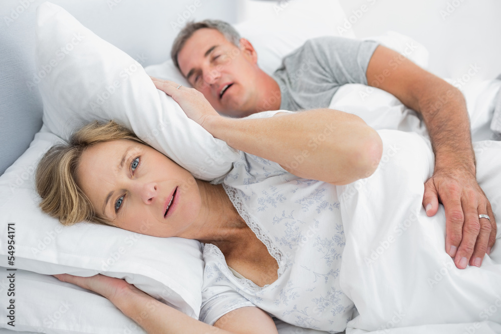 Irritated wife blocking her ears from noise of husband snoring Irritated wife blocking her ears from noise of husband snoring