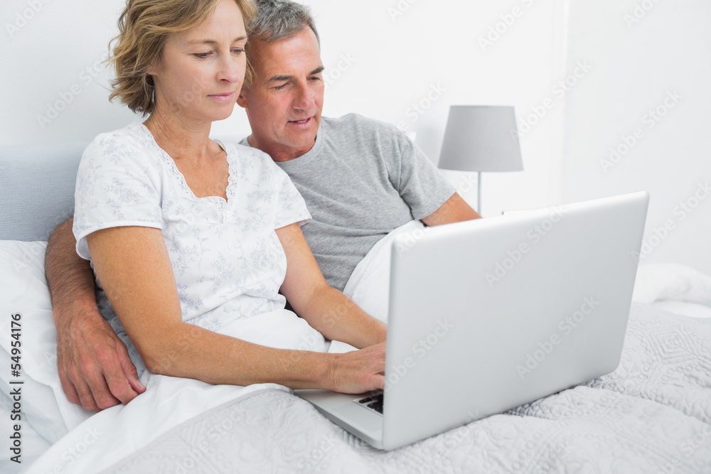 Happy couple using their laptop together in bed