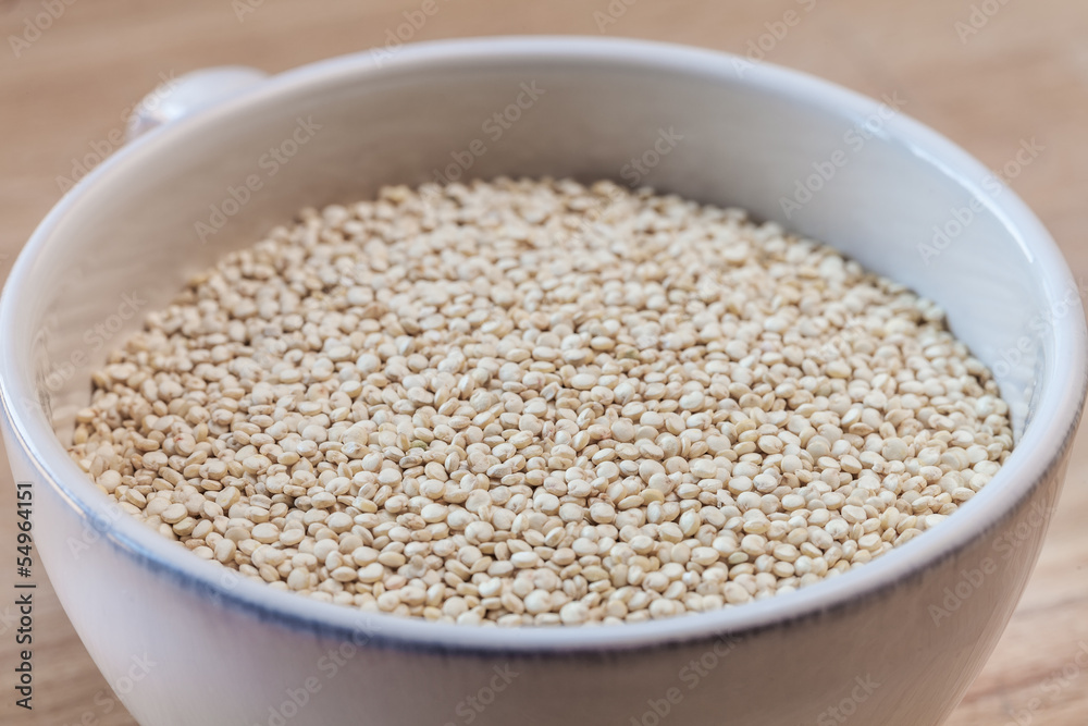Raw organic quinoa seeds in white cup on wooden board background Raw organic quinoa seeds in white cup on wooden board background