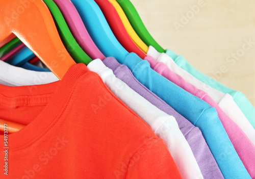 Different shirts on colorful hangers on light background