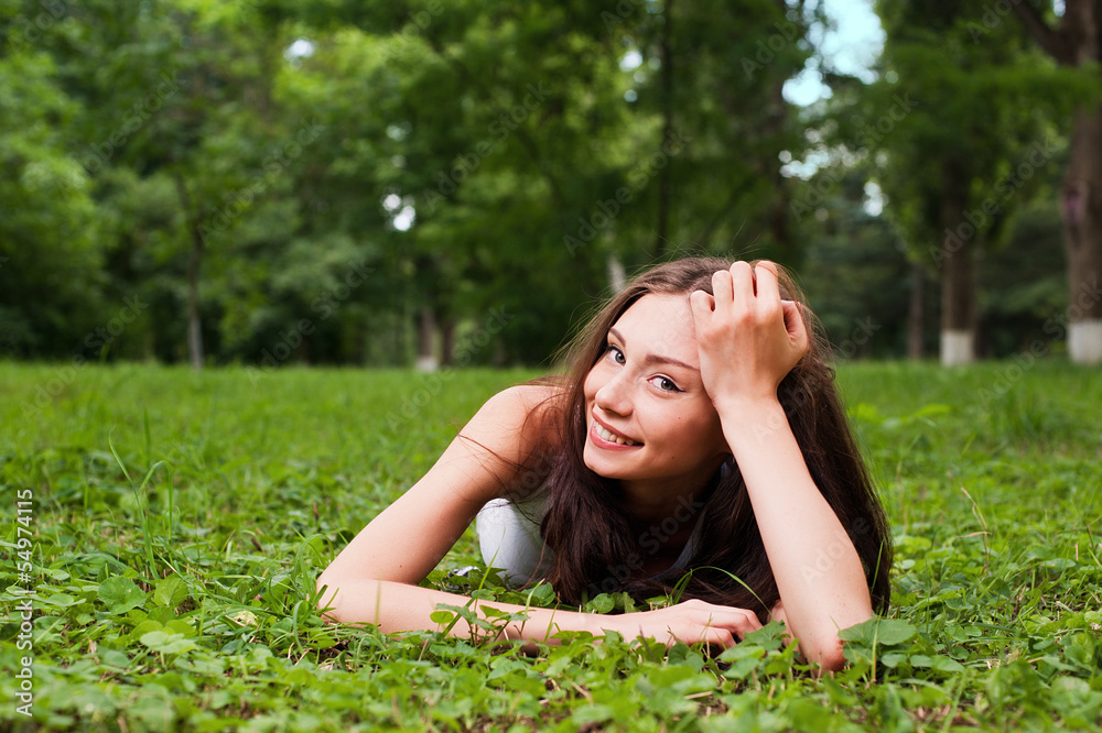 Smiling young woman lying on green grass Smiling young woman lying on green grass