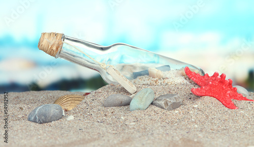 Glass of bottle with note inside on bright blue background