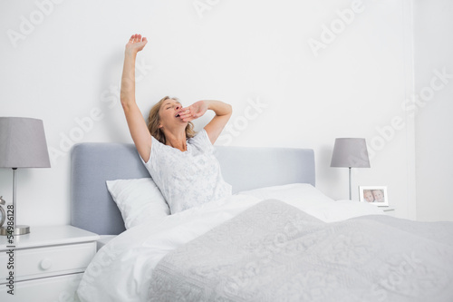 Blonde woman stretching and yawning in bed in the morning