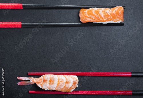 close-up of chopsticks and two sushi with salmon and shrimp