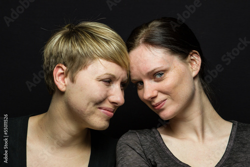 Lesbian couple posing against black background, horizontal