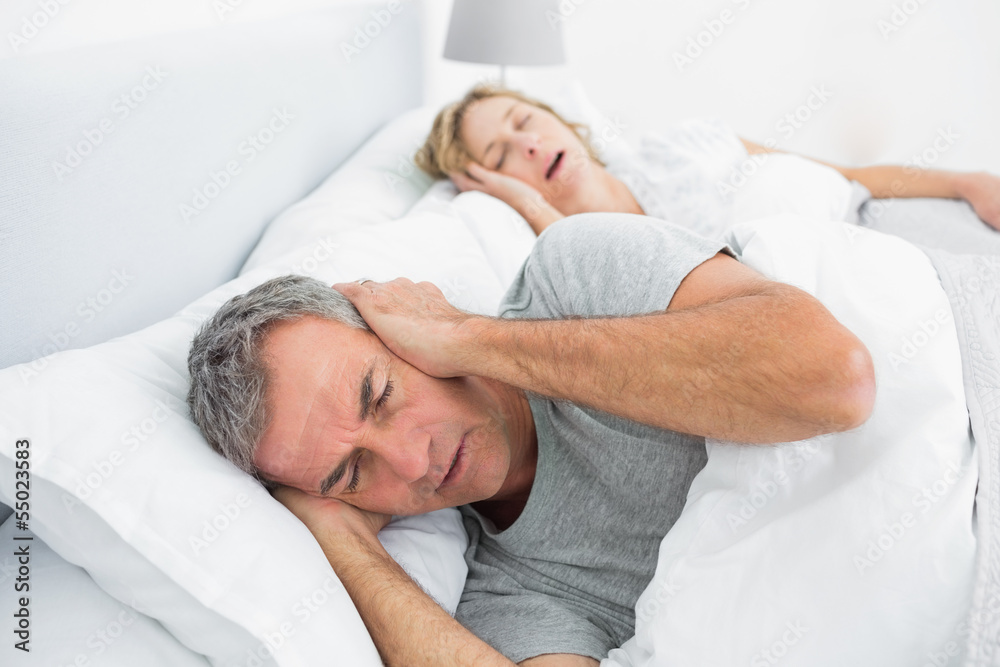 Tired man blocking his ears from noise of wife snoring Tired man blocking his ears from noise of wife snoring