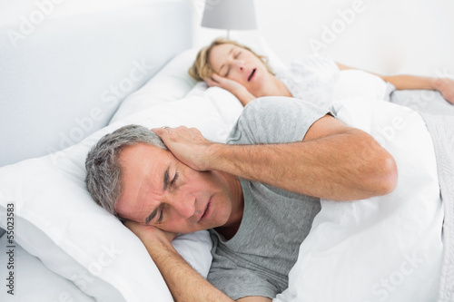 Tired man blocking his ears from noise of wife snoring