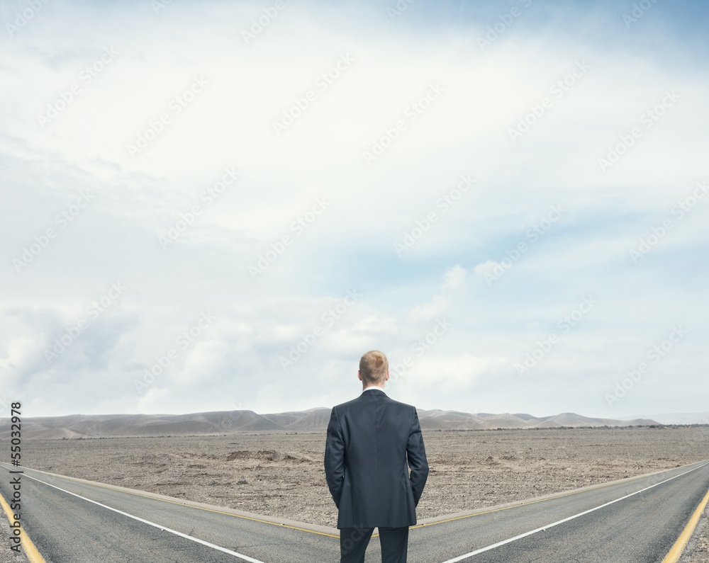 businessman standing in front of two roads businessman standing in front of two roads