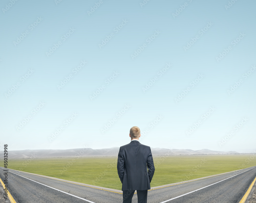 businessman standing in front of two roads businessman standing in front of two roads