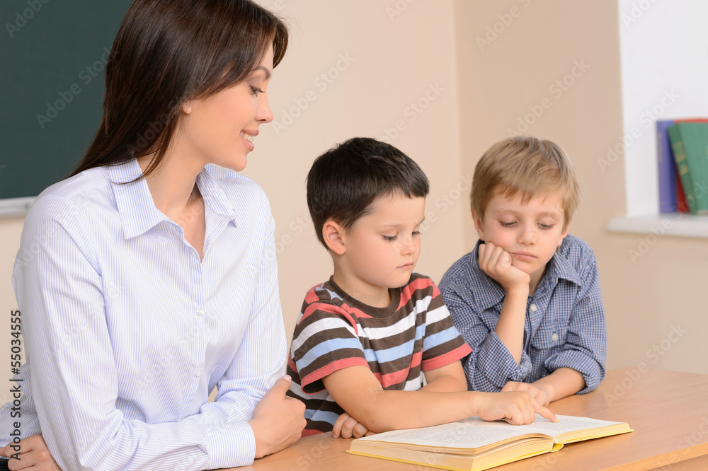 Reading together. Cheerful young female teacher sitting near two Reading together. Cheerful young female teacher sitting near two