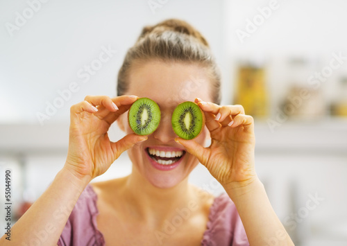 Smiling young woman holding kiwi slices in front of eyes