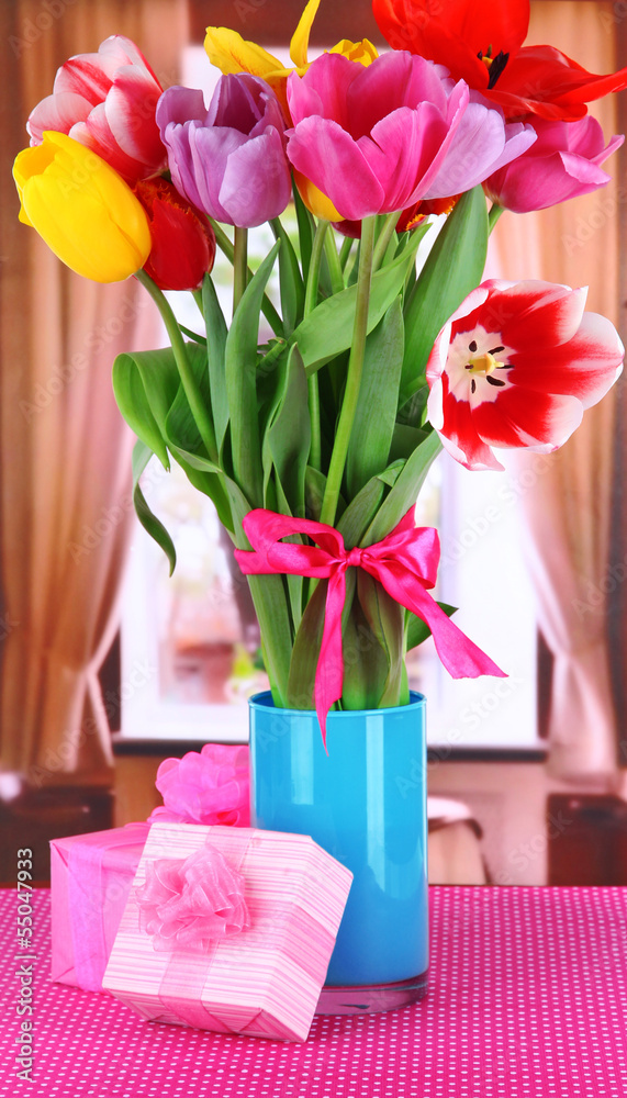 Beautiful tulips in bouquet with gifts on table in room Beautiful tulips in bouquet with gifts on table in room