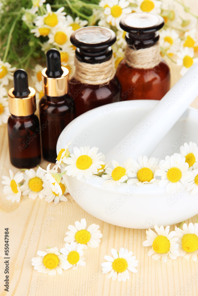 Essential oil and chamomile flowers in mortar on wooden table Essential oil and chamomile flowers in mortar on wooden table