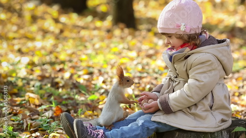 Happy child feeds a little squirrel in autumn park