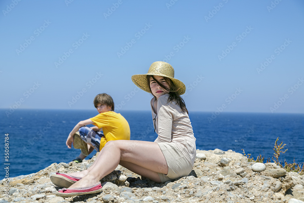 two teens sitting on the top of a mountain with blue ocean in ba
