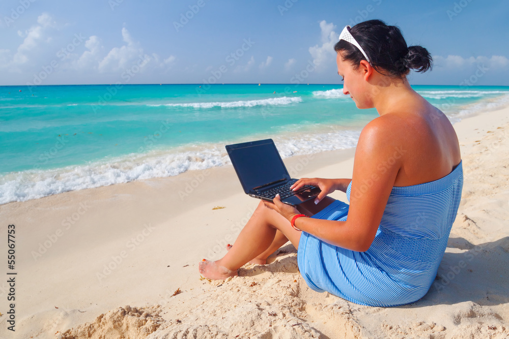 Woman with laptop sitting at the Caribbean sea