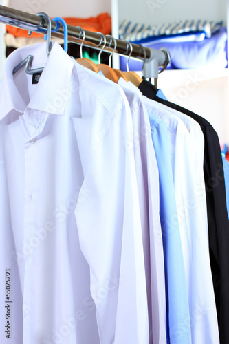 Variety of casual shirts on wooden hangers on shelves