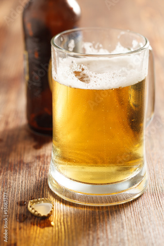 cold beer glass on bar or pub desk, bottle of beer on background