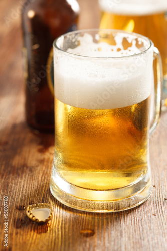 cold beer glass on bar or pub desk, bottle of beer on background