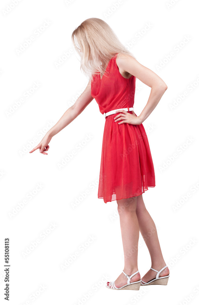 Back view of young blonde woman pointing at wall.