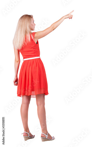 Back view of young blonde woman pointing at wall.