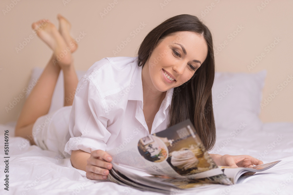 Woman reading magazine. Beautiful young woman in white shirt lyi