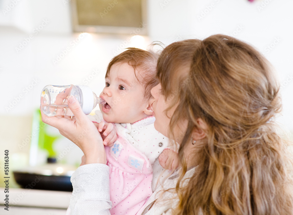 Mother feeding baby with feeding bottle in kitchen Mother feeding baby with feeding bottle in kitchen