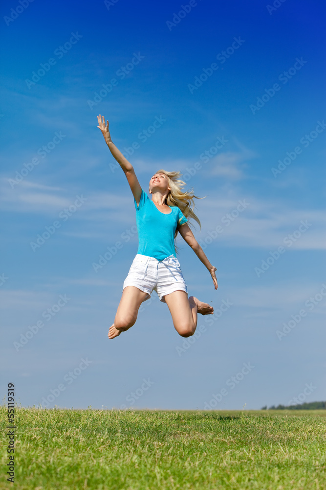 The happy woman jumps in summer green field against blue sky The happy woman jumps in summer green field against blue sky