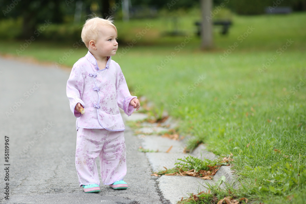 Adorable baby girl in kimono walks on a street next to a park Adorable baby girl in kimono walks on a street next to a park